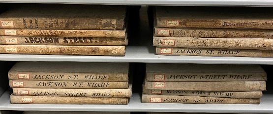 Rows of bound nineteenth- and early twentieth-century ledgers labeled Jackson Street Wharf on an archive shelf.